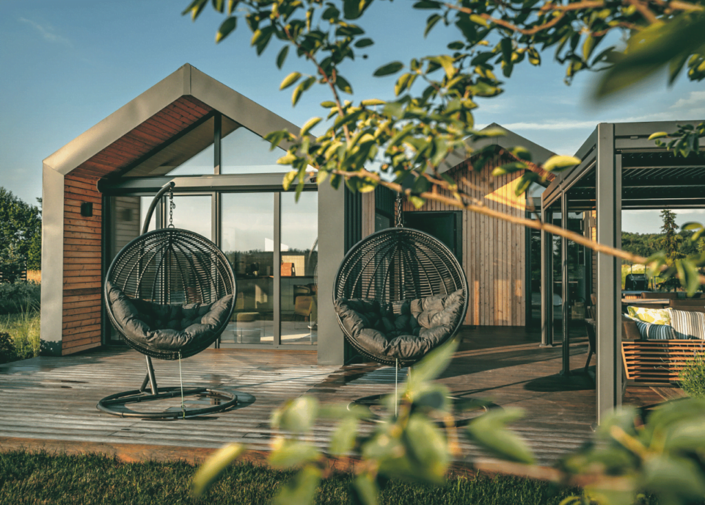 tiny house vanuit de bosjes gefotografeerd, hangede tuinstoelen, houten terras