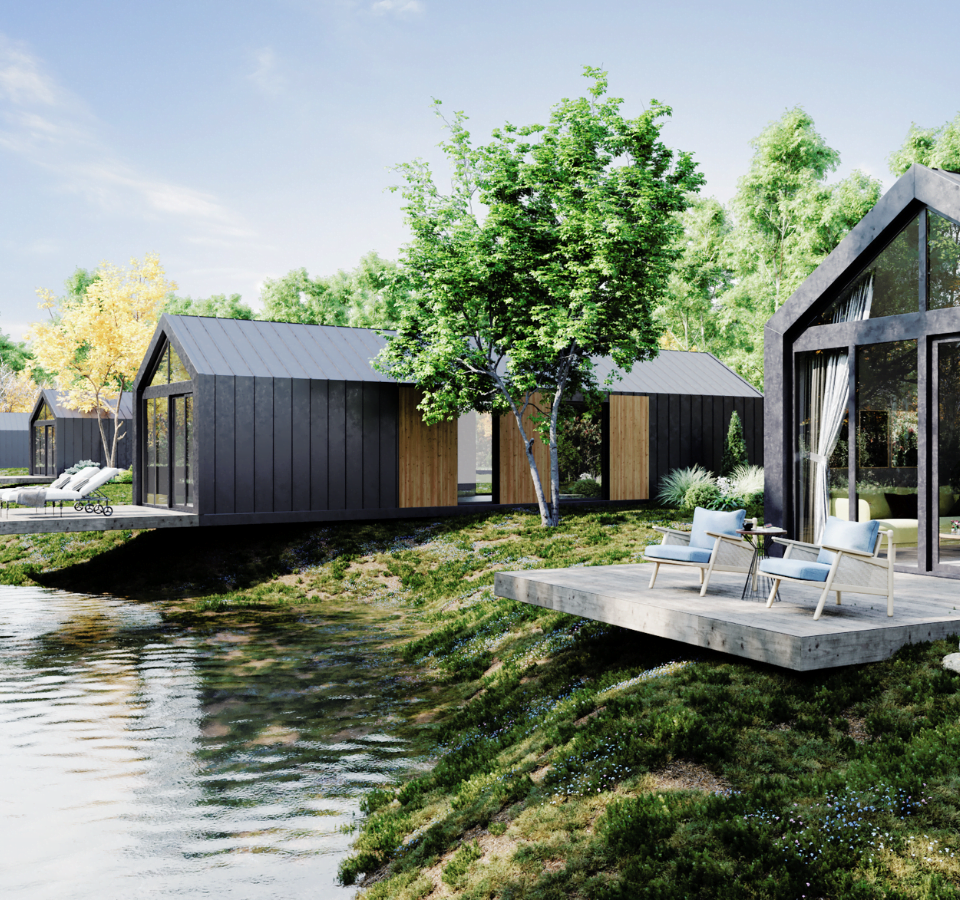 De Malmö XL, het langste Tiny Home uit de serie, staat aan de waterkant met een groot terras, moderne buitenmeubels en omringd door weelderige bomen en een helderblauwe hemel.