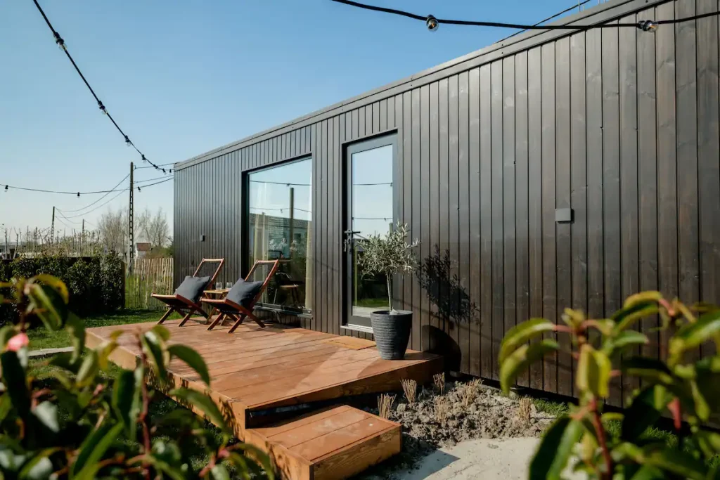 prefab tiny house met houten terras, sfeer verlichting, groene planten