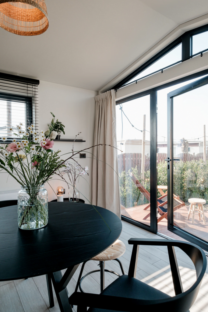 tiny house keuken en woonkamer, zwarte tafel met stoelen, glazen voorgevel met beige gordijnen 