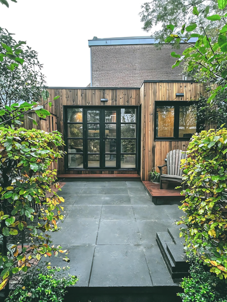 Exterieur van een modern huis met houten bekleding en grote glazen deuren, omgeven door weelderig groen