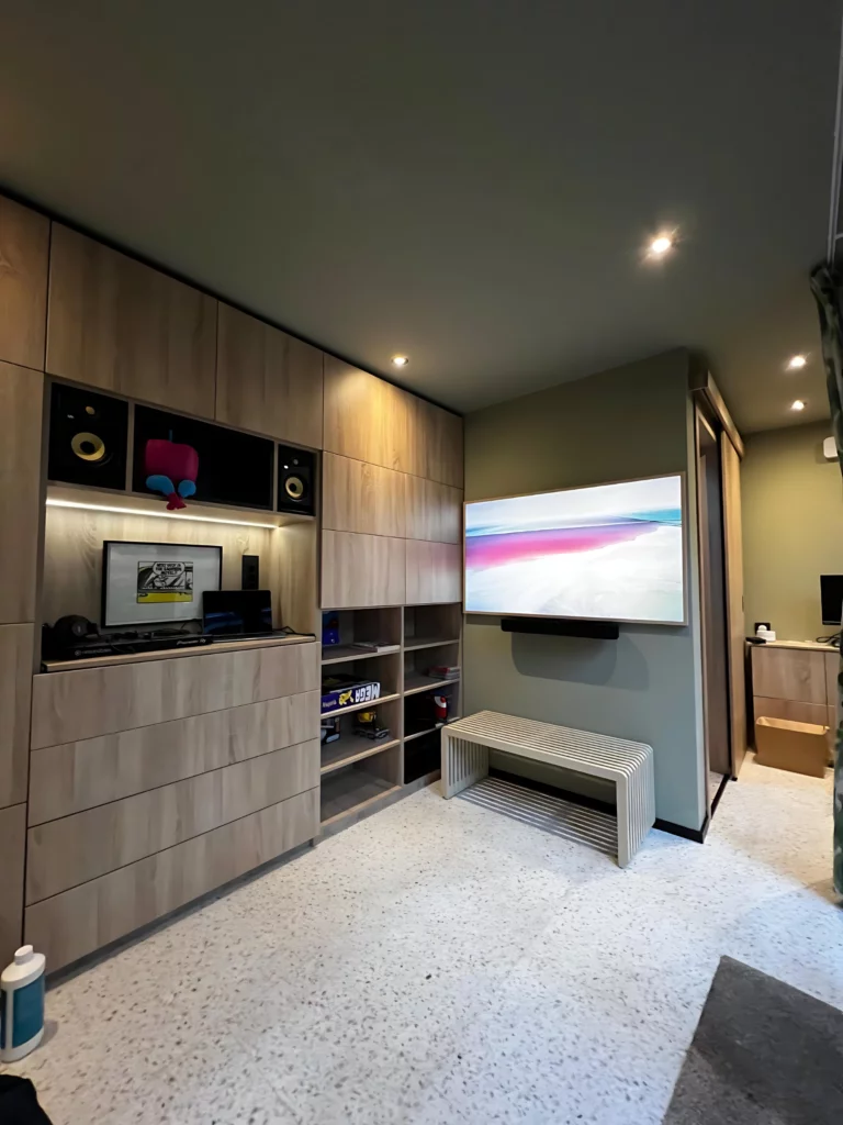 Binnenkijk in een modern huis met een mediawand, inclusief een grote flatscreen-tv en ingebouwde planken.