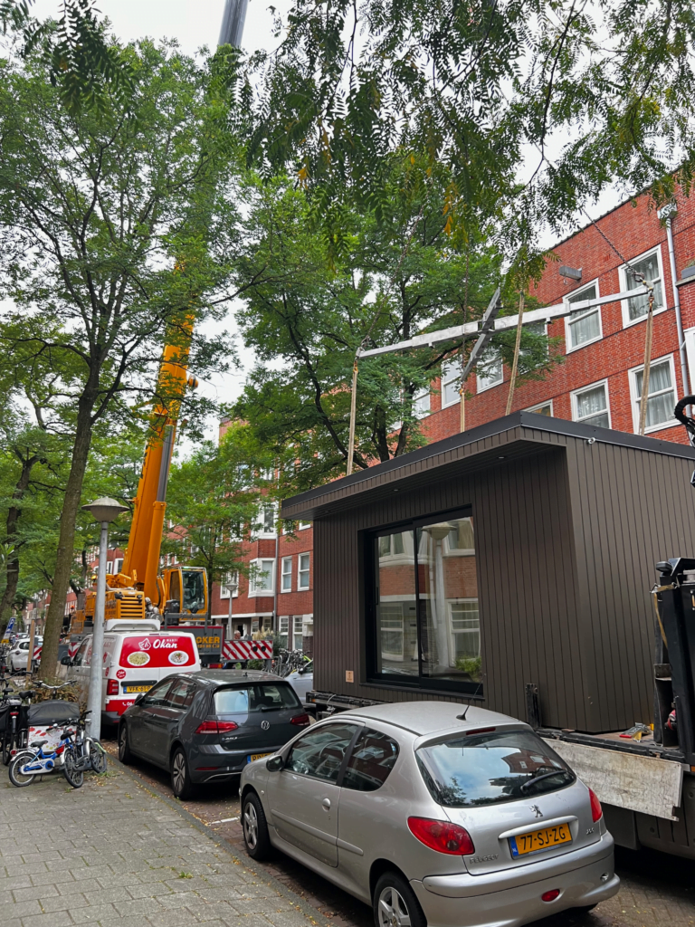 Stedelijke installatie van een modulair huis met een grote hijskraan in een met bomen omzoomde straat