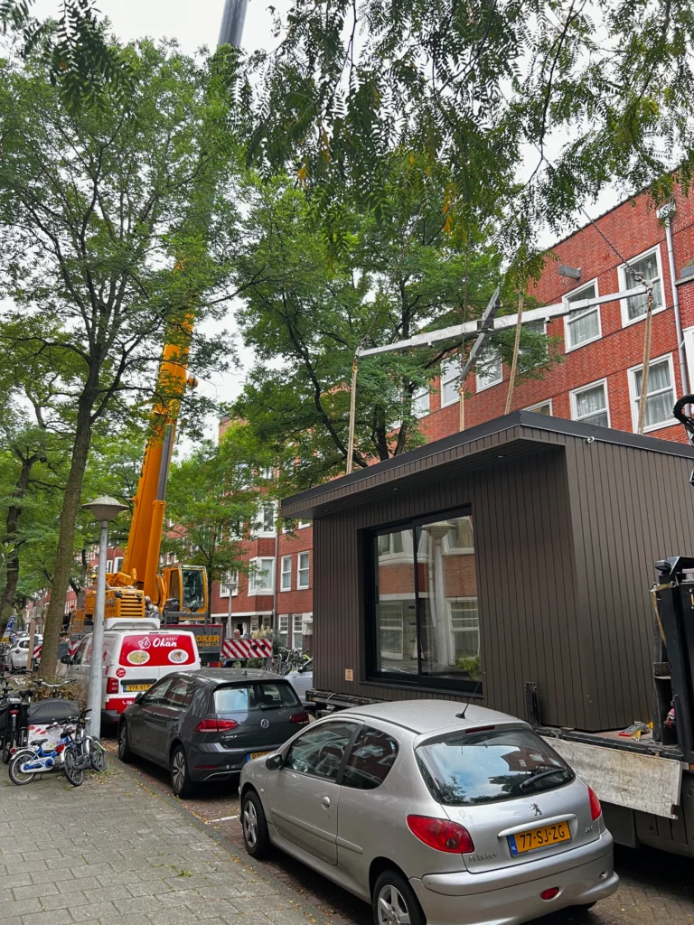 Stedelijke installatie van een modulair huis met een grote hijskraan in een met bomen omzoomde straat