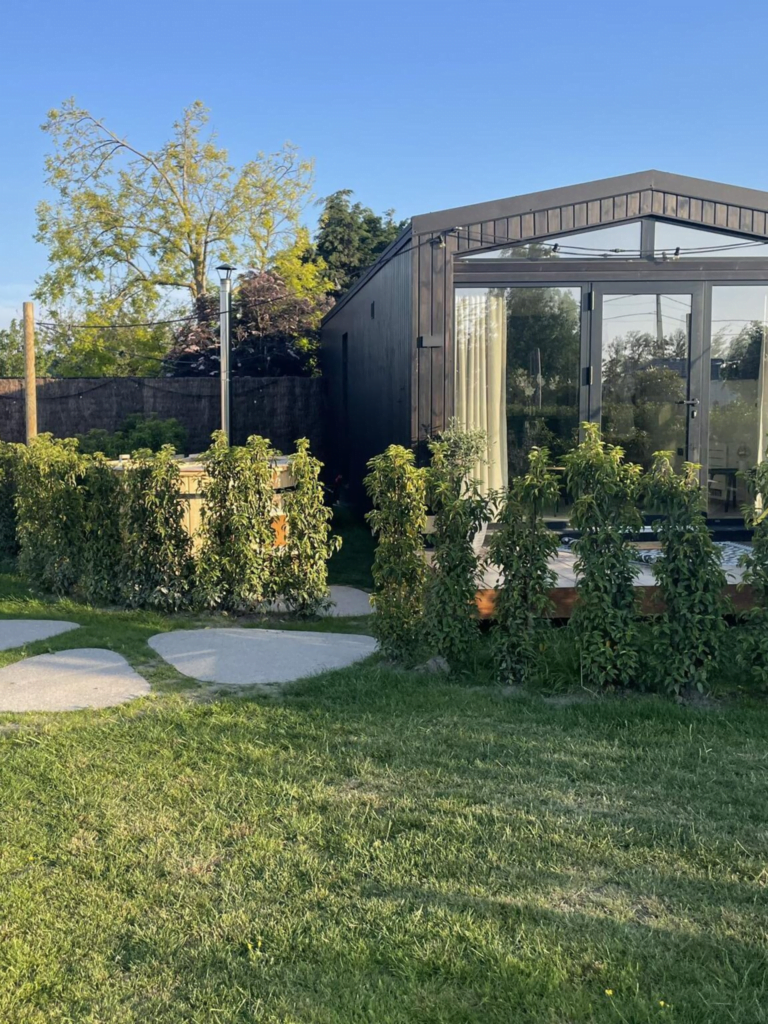 Luxe tuinhuis met volledige glazen wanden en deuren, omringd door een goed onderhouden tuin met paden en plantenbakken