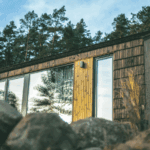 Een tijdelijk Tiny House op een flexibele schroefpalenfundering in de gemeente Steenwijkerland, geschikt voor plaatsing tot 15 jaar. De woning heeft een houten gevel met grote raampartijen en staat tegen de achtergrond van een dennenbos